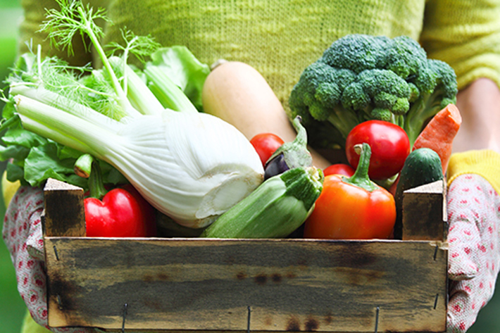 Person holding a wooden box of fresh spring vegetables.
